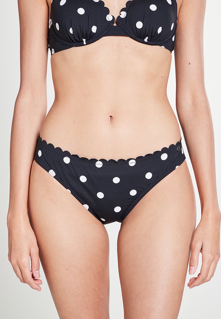 Ensemble de bikini noir à pois blancs. Le soutien-gorge présente des bords festonnés ; le bas a un design et une coupe similaires, mettant en valeur le motif.