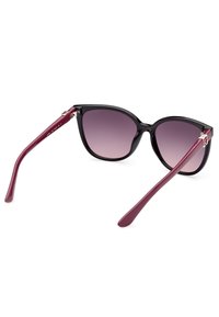 Lunettes de soleil en forme de chat avec des montures noires et des verres dégrad�és violets. Les branches sont bordeaux, avec un détail métallique près de la charnière.