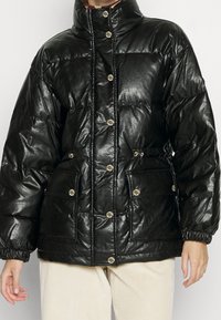 Czarna kurtka puchowa z wysokim kołnierzem, błyszczącą teksturą, zatrzaskami, elastycznymi mankietami i dwoma przednimi kieszeniami. Posiada taliowany fason.