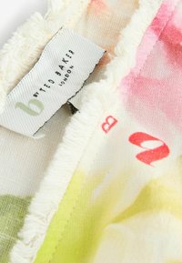 Lillekiri mustriga kangas, millel on pehme tekstuur, sisaldades roosa, rohelise ja kollase toone. Sildil on kiri "b by Ted Baker London." Äärtes on kulunud servad.