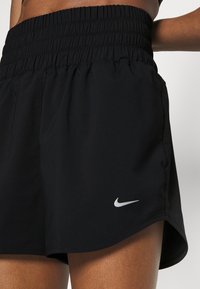 Mustat urheilushortsit, jotka on valmistettu kevyestä kankaasta ja joissa on teksturoitu, joustava vyötärö. Alareunassa on pieni valkoinen Nike-logo.
