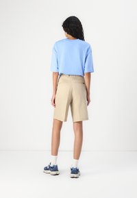Un t-shirt bleu à manches courtes associé à un short beige. Le short a une coupe décontractée et deux poches arrière. Porté avec des baskets bleues et des chaussettes blanches.