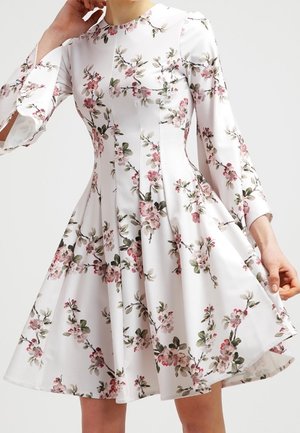 Sukienka w kwiaty z długimi rękawami, wykonana z lekkiego materiału. Posiada okrągły dekolt, różowo-zielony wzór kwiatowy na białym tle oraz rozkloszowaną spódnicę.
