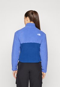 Fleece jakna u svijetloplavoj i tamnoplavoj boji. Visoki ovratnik, dugi rukavi i logo na poleđini. Mekana tekstura i dizajn s blokiranjem boja.