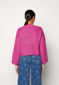 Gekürzter, rosa gestrickter Pullover mit Rippmuster und weiten Ärmeln, kombiniert mit Jeanshosen mit einem Frieden-Zeichen-Muster.