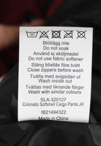 Etiket for Colorado Softshell Cargo Bukser JR; indeholder vaskeanvisninger på flere sprog; hvid baggrund med sort tekst; inkluderer nogle ikoner.