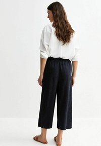 Pantalons larges à rayures marines avec ceinture élastique, associés à une chemise blanche ample. Texture lisse, coupe à la cheville, style décontracté.
