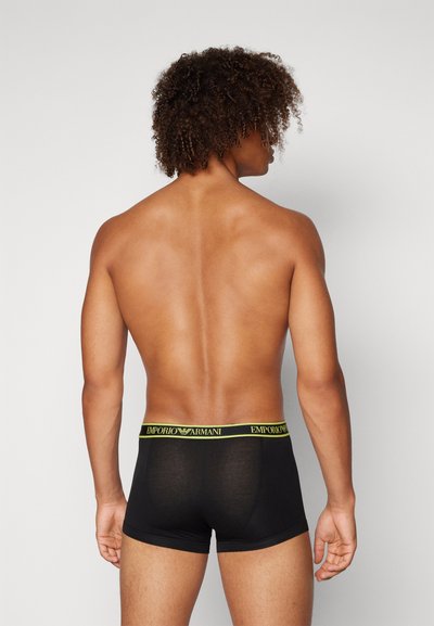 Boxer breif neri con una vestibilità snug, caratterizzati da un elastico in vita con logo giallo. Il tessuto appare morbido e leggermente elastico.