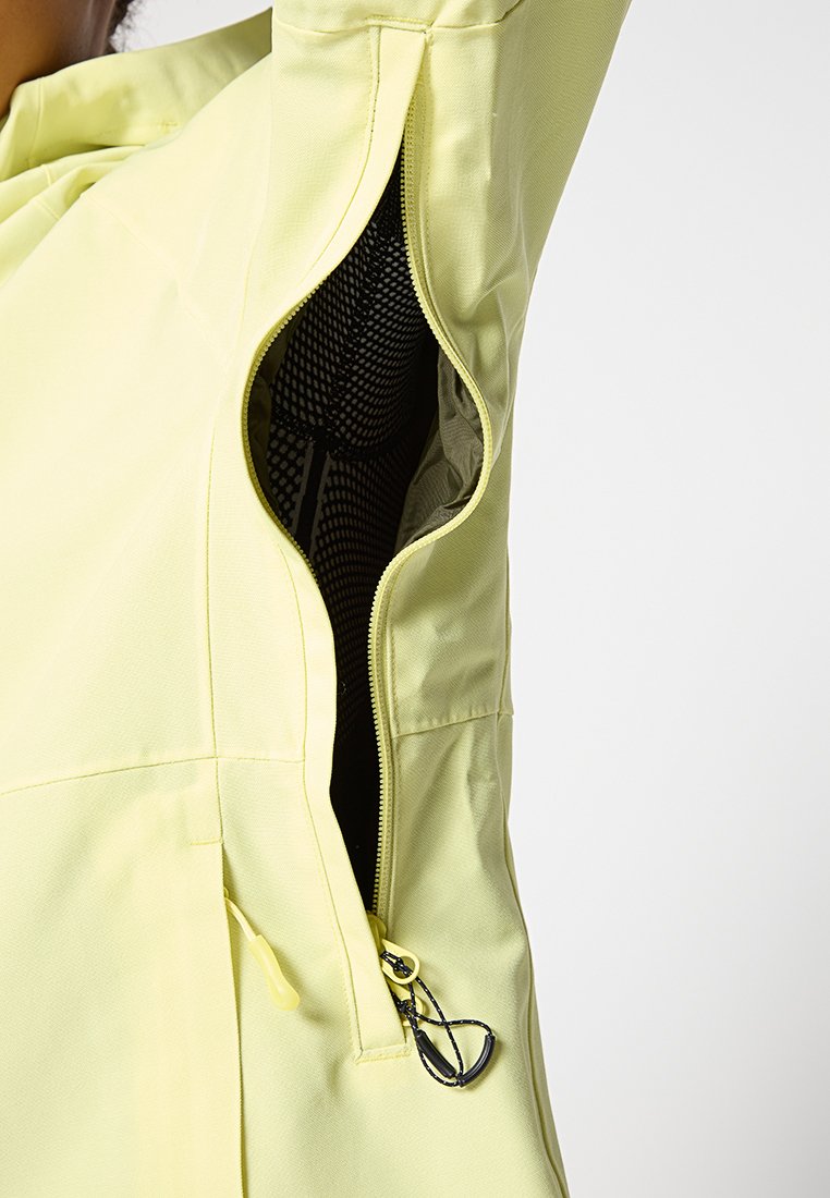 Chaqueta amarilla con ventilación en la axila con cremallera abierta que muestra un forro de malla negra y un cordón interior.