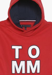 Roter Kapuzenpullover aus Baumwolle mit dunkelblauer Innenfütterung, vorne mit großen weißen Buchstaben "TOMM" und einer Kapuze mit Kordelzug.