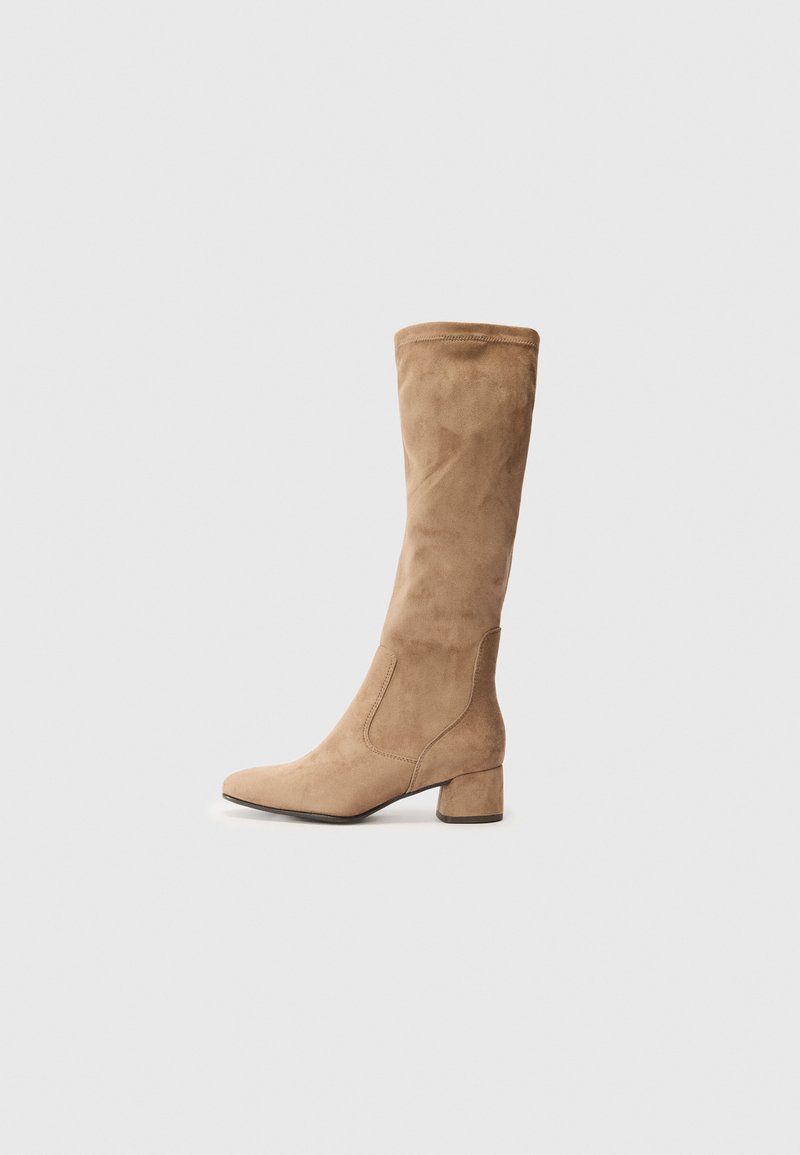 Botte en suède beige monter jusqu'au genou avec un bout pointu et un talon bloc. Présente des coutures sur les côtés et une texture lisse. Design simple et minimaliste.
