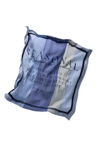 Carré de tissu rayé bleu et blanc avec le texte "SEASONAL Remain or Evolve" et une bordure en pointillés, délicatement plié sur fond blanc.