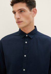 Donkerblauwe button-up shirt met een gestructureerde kraag en zes witte knoopsluitingen. Glad textuur en een getailleerde pasvorm.