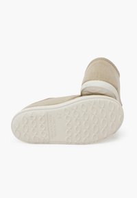 Scarpa slip-on in tela beige con parte superiore in tessuto testurizzato e suola in gomma bianca. Presenta un motivo ondulato sulla suola e un’etichetta interna.