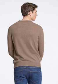 Brun stickad tröja med rund hals och långa ärmar, med en slät yta. Kombinerad med blå denimjeans. Sedd bakifrån.