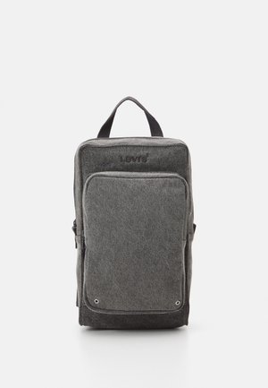 Grijze stoffen rugzak met rechthoekige vorm, voorzien van een voorvak met rits, bovenste handvat en subtiele logo-embossing aan de bovenkant.