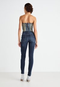 Denim korzet gornji dio s plavim vertikalnim prugama, uparen s tamnim uskim trapericama. Ima nisku leđa i srebrne čizmice na visoku petu.