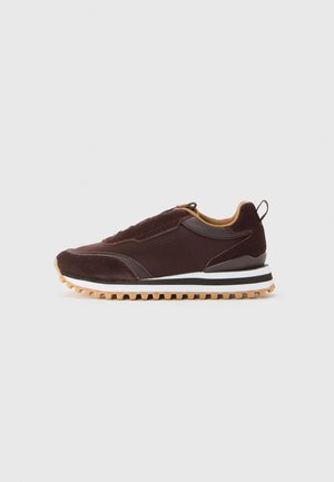 Baskets marron foncé avec des panneaux en daim et en cuir, doublure intérieure beige, semelle rayée blanche et noire, et semelle en caoutchouc naturel, vue de côté.