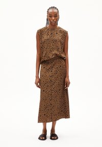Brown sleeveless top and long skirt with black spots, made of soft fabric. Paired with black slide sandals. Simple, unadorned design.
