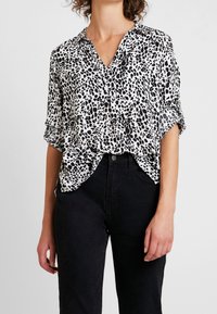 Blusa a stampa leopardata in bianco e nero con maniche corte, colletto e vestibilità rilassata, abbinata a jeans neri a vita alta.