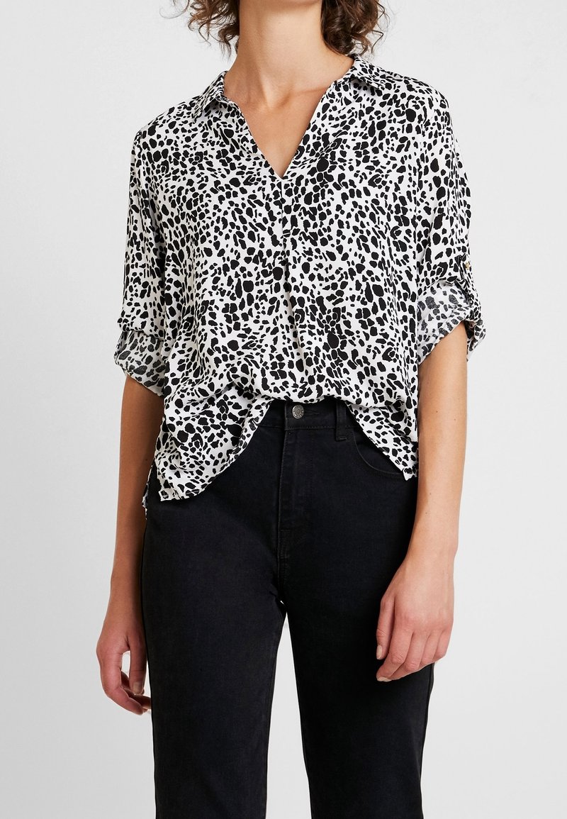 Blusa a stampa leopardata in bianco e nero con maniche corte, colletto e vestibilità rilassata, abbinata a jeans neri a vita alta.