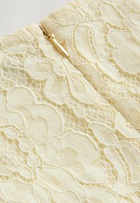 Peene kangas pehmes kollases toonis, millel on lillemotiivid ja õrn tekstuur. Õmblusel on nähtav läikiv kuldne tõmblukk.