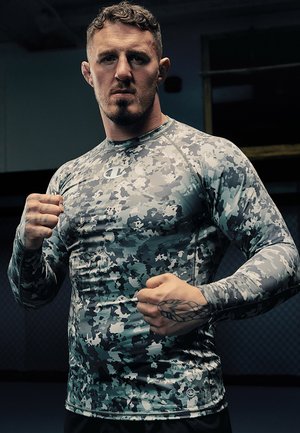 Camisa athletic de manga larga en patrón de camuflaje gris, fabricada con material elástico y un diseño ajustado, con costuras reforzadas y un logo circular.