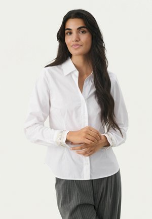 Camicia bianca con colletto, polsini decorati con paillettes, vestibilità sagomata e maniche lunghe, abbinata a pantaloni grigi a righe.