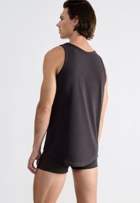 Débardeur noir sans manches en tissu doux, avec un ourlet arrondi et une coupe décontractée, associé à un short foncé assorti.