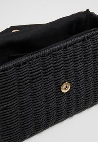Borsa a tracolla intrecciata nera realizzata in materiale testurizzato, con chiusura a bottone a pressione dorato e interno in tessuto nero.