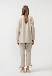 Béžový lněný outfit skládající se z volnějšího topu a zúžených kalhot se bočními rozparky, doplněný obuví neutrální barvy.