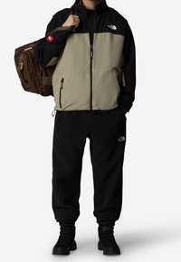 Letvægtsfarveblockeret jakke i beige og sort med lynlåslommer. Sorte fleecebukser og robuste sorte støvler. Brun rygsæk inkluderet.