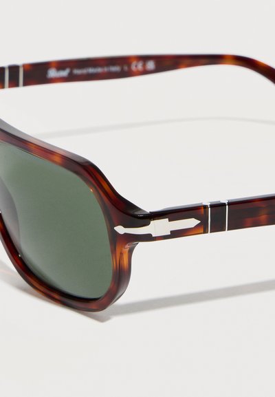 Γυαλιά ηλίου με σχέδιο χελώνας, με ορθογώνιους φακούς σκούρου πράσινου χρώματος και ασημένια λεπτομέρεια σε σχήμα σπαθιού στο πλαίσιο του βραχίονα.