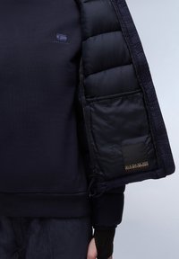 Granatowy sweatshirt z pikowanym, puszystym czarnym wykończeniem, z małym logo na piersi i metką na rękawie. Teksturowany materiał z gładkimi akcentami.