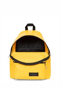 Mochila amarilla con cremallera y forro negros. Cuenta con un compartimento principal con un bolsillo frontal, un asa en la parte superior y un parche con el logo.
