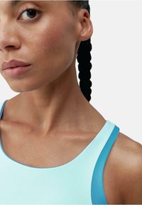 Tricou sport lejer de culoare albastru deschis cu accente albastre, având un gât adânc și bretele subțiri, prezentat pe o piele cu o textură netedă și uniformă.