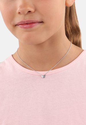 Silberne, schmetterlingsförmige Halskette an einer dünnen Kette, getragen über einem hellrosa strukturierten Hemd. Nahaufnahme auf den Hals und die Details des Anhängers.