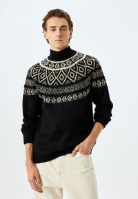 Zwarte gebreide coltrui met een fair isle patroon in crème over de borst en schouders, met geribde mouwen en zoom.