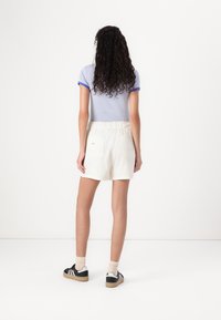 Haut à manches courtes rayé bleu clair, short blanc à taille élastique avec poches, baskets noires avec accents blancs, chaussettes mollet beiges.