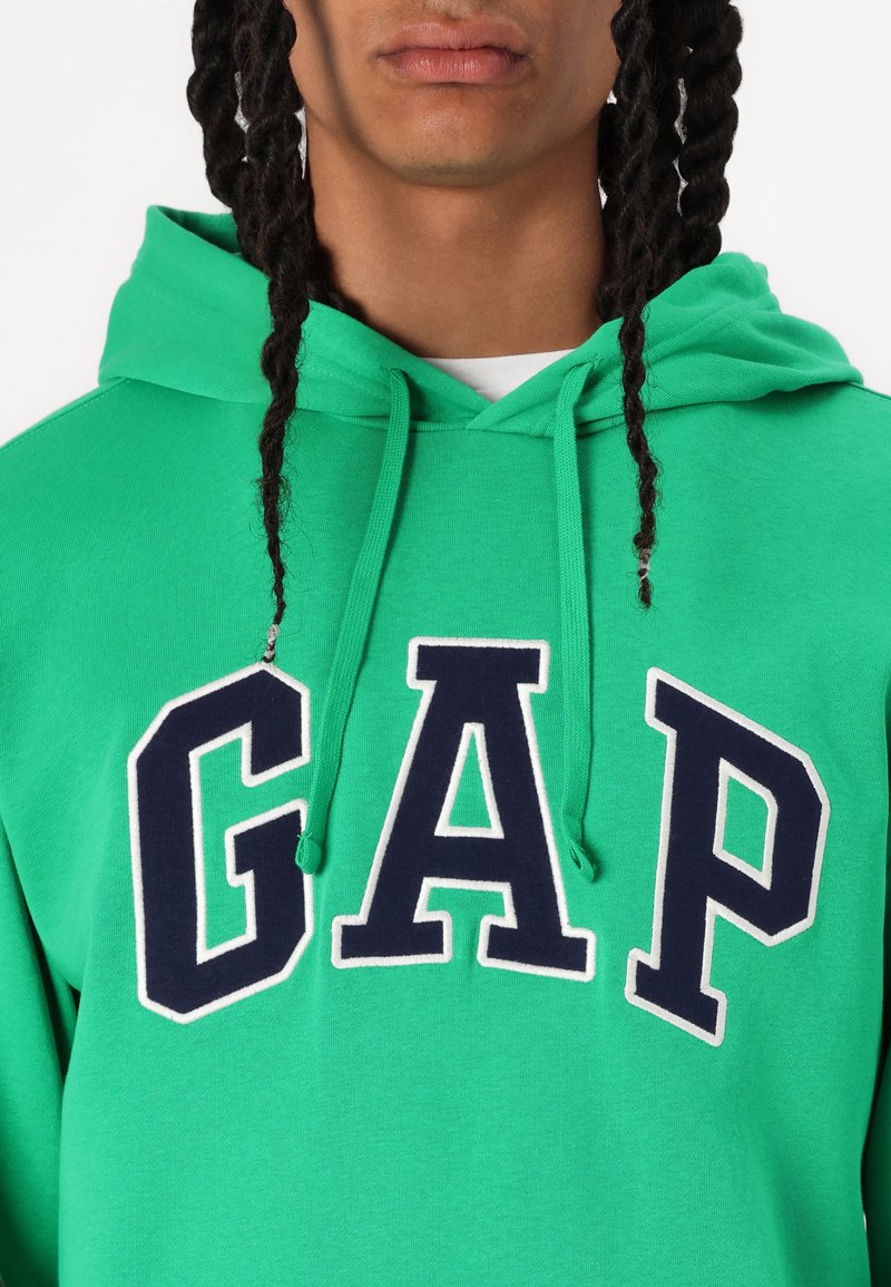Grüner Baumwoll-Hoodie mit großem navyblauen "GAP"-Logo, umrandet in Weiß, mit Kordeln an der Kapuze und gerippten Bündchen.