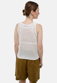 Débardeur blanc en tricot avec un design en maille, dotée d'un décolleté rond et d'un ourlet légèrement arrondi. Porté avec un short en lin marron.
