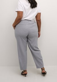 Pantalones de tela grises con un corte relajado, cintura elástica y dos bolsillos traseros. Combinados con sandalias negras de tacón.