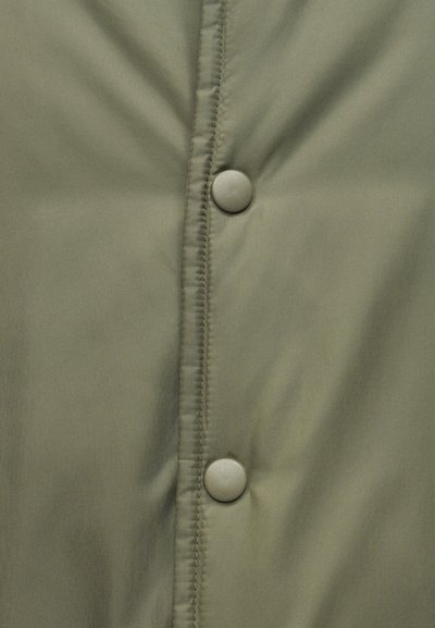 Tissu vert olive mat avec deux boutons-pression ronds alignés verticalement le long d'une couture avec surpiqûres.