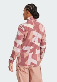 Sudadera de forro polar en tonos rosas con patrones geométricos abstractos. Cuello alto y mangas largas, con una textura suave y un corte relajado.