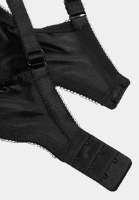 Sort bh med glat stof, justerbare stropper og lukning med hægte. Kantet med fine, bølgede kanter.