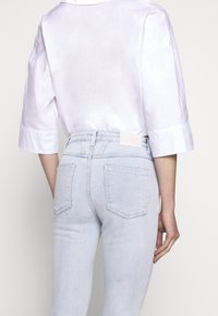 Blusa lila claro con mangas tres cuartos combinada con jeans ajustados azul claro que tienen bolsillos traseros y una cinturilla con marca.
