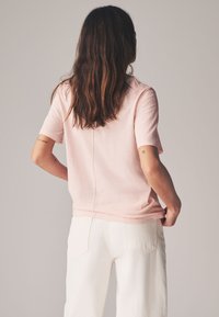 Kortärmad, ljusrosa T-shirt i mjukt tyg med avslappnad passform och sömdetalj bak, kombinerad med vita jeans.