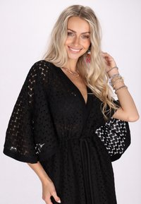 Fekete, nyitott elülső, kimono stílusú takaró, texturált mintával, megkötős derekú, széles ujjakra jellemző kontrasztos belső mintázattal.