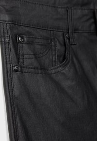 Pantalon en denim noir avec une poche avant à bouton, des coutures distinctes et une texture lisse. Mettez l'accent sur les détails et la couleur sombre.