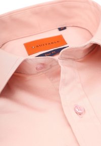 Slim fit shirt in lichtroze stof, met een spread collar, twee knopen en labels met de tekst "Geschikt" en "Slim Fit" in contrasterende kleuren.